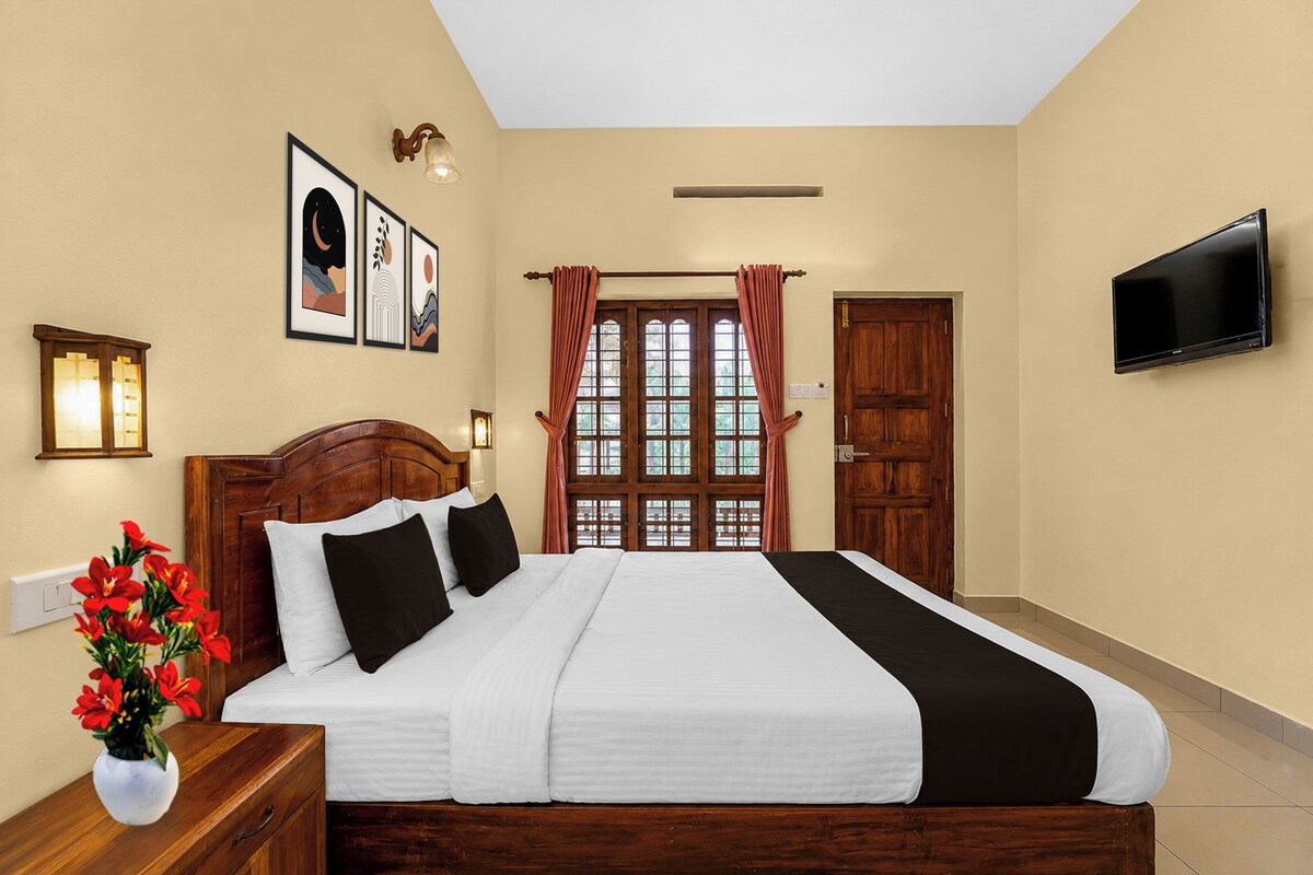A hotel room with a large bed, a flat-screen TV mounted on the wall, and a window with curtains.
