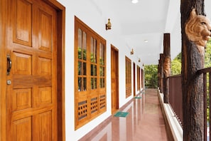 A corridor with wooden doors and windows, a polished floor, and a decorative tree trunk. - Collection O Elephant Camp Thekkady (Thekkady)