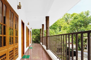 A corridor with wooden doors and a balcony with a metal railing overlooking a lush green area. - Collection O Elephant Camp Thekkady (Thekkady)