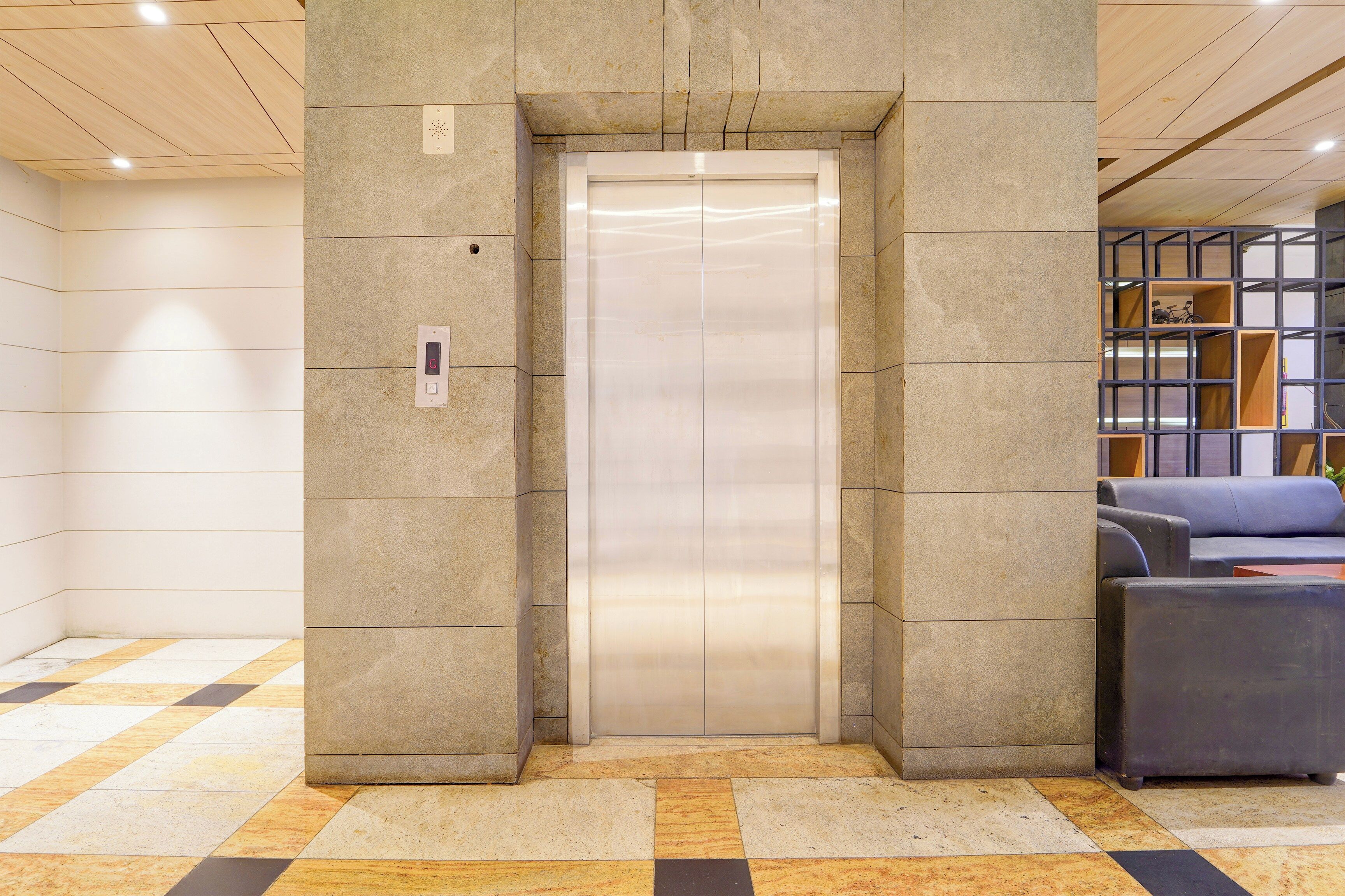 An elevator in a lobby with a checkered floor pattern and a seating area with a blue sofa.