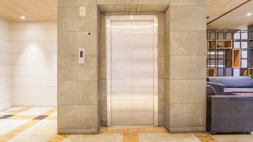 An elevator in a lobby with a checkered floor pattern and a seating area with a blue sofa.