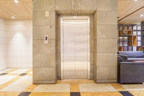An elevator in a lobby with a checkered floor pattern and a seating area with a blue sofa.