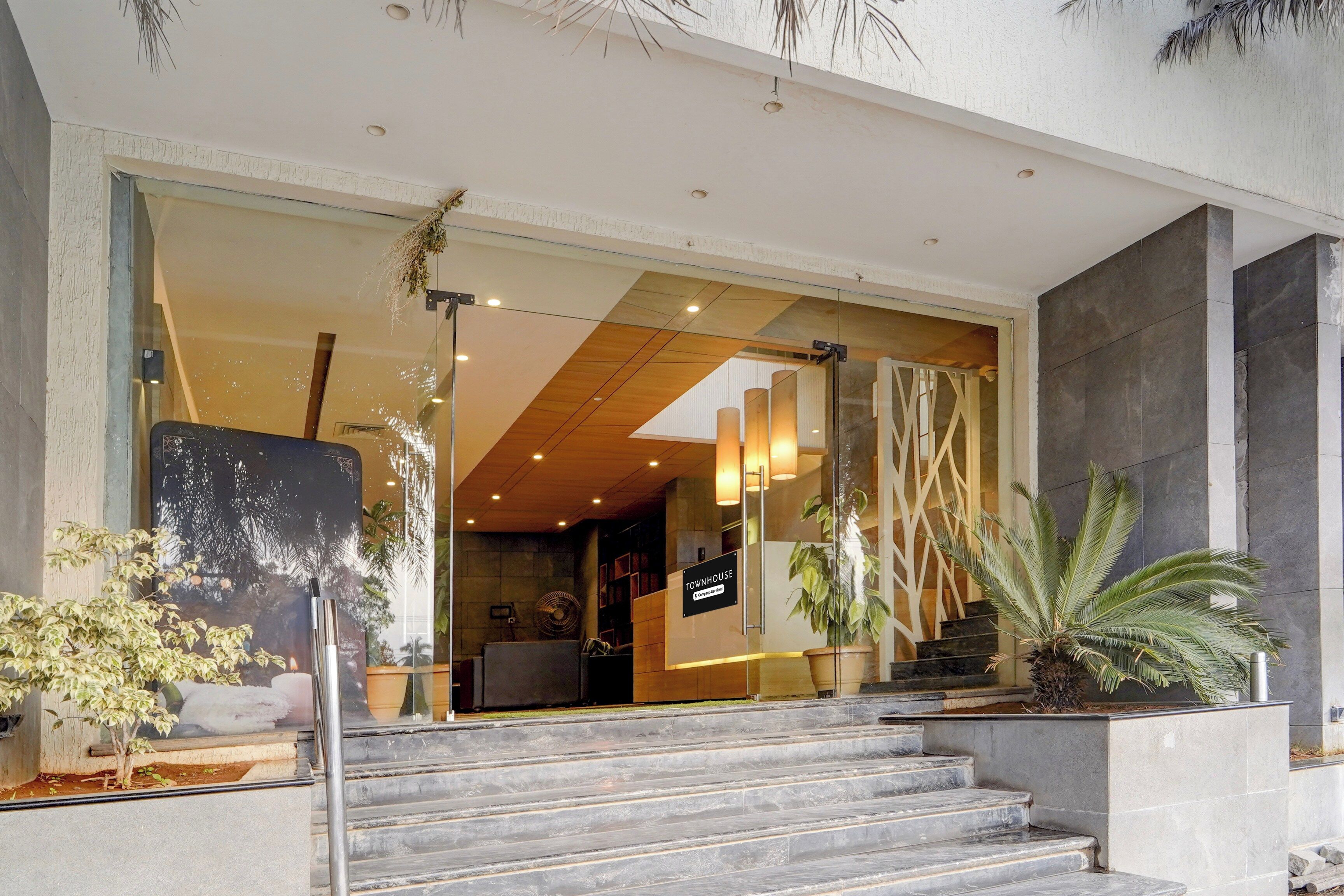 A modern building entrance with a glass facade, a staircase leading to the entrance, and potted plants.
