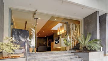 A modern building entrance with a glass facade, a staircase leading to the entrance, and potted plants.