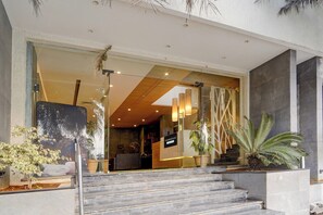 A modern building entrance with a glass facade, a staircase leading to the entrance, and potted plants.