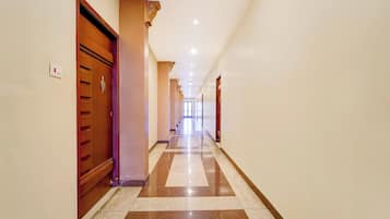 A hotel corridor with wooden doors, a checkered floor, and a light switch on the wall.