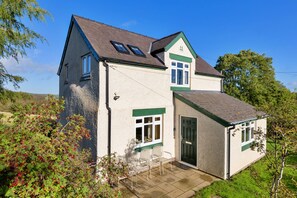A two-story house with a sloped roof, a visible chimney, and a small porch with chairs. - Finest Retreats | Ffrith-Bach (Abergele)