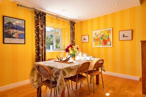 A dining area with a table set for four, surrounded by wicker chairs, a floral tablecloth, and a vase of flowers. - Finest Retreats | Ffrith-Bach (Abergele)