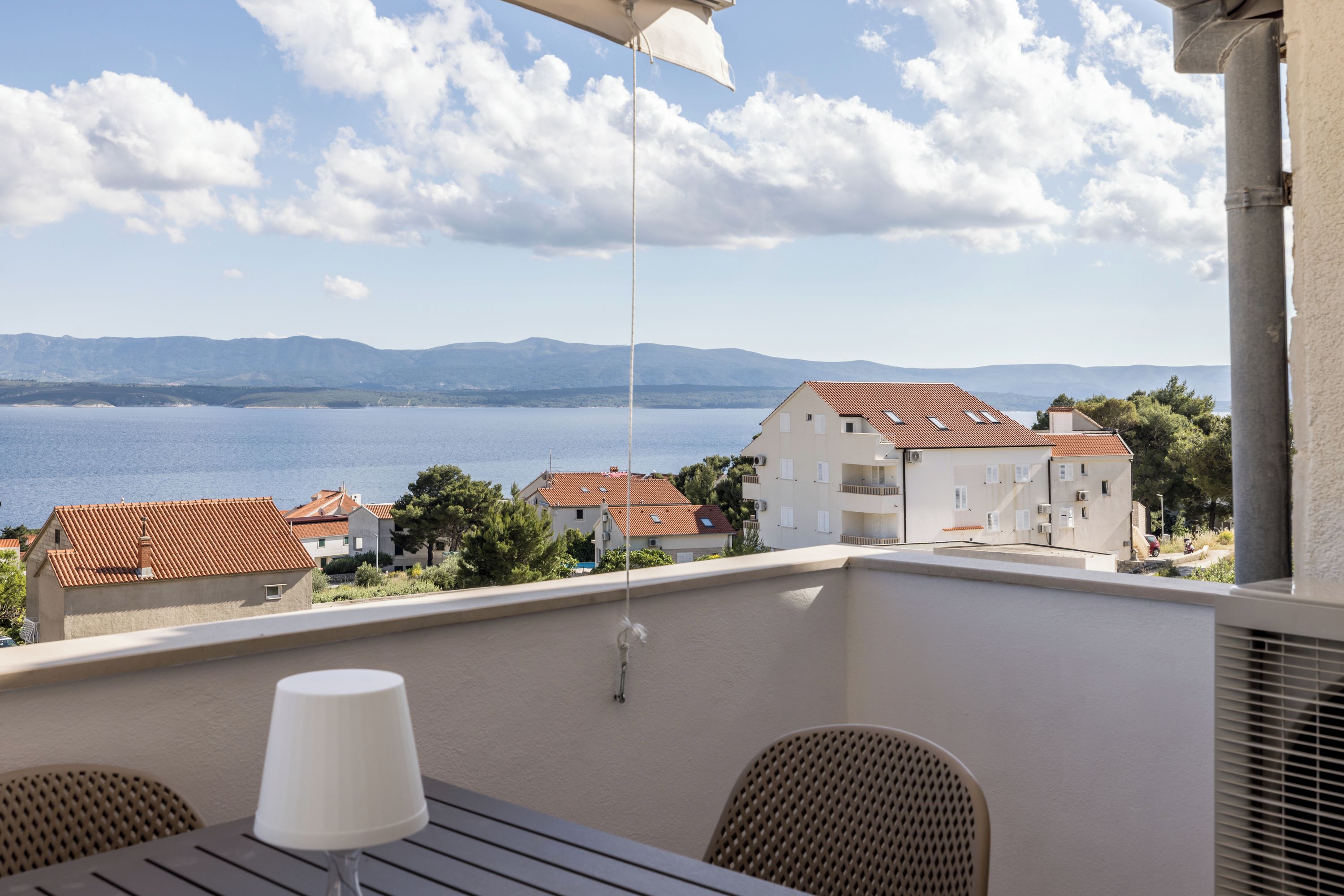 A balcony with a table and chairs, overlooking a body of water and buildings.