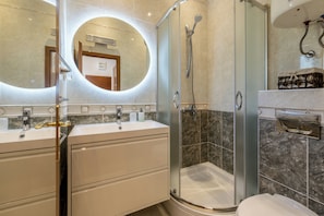 A modern bathroom with two sinks, a glass-enclosed shower, and a marble-tiled wall. - Bolotel family & studio stay (Bol)