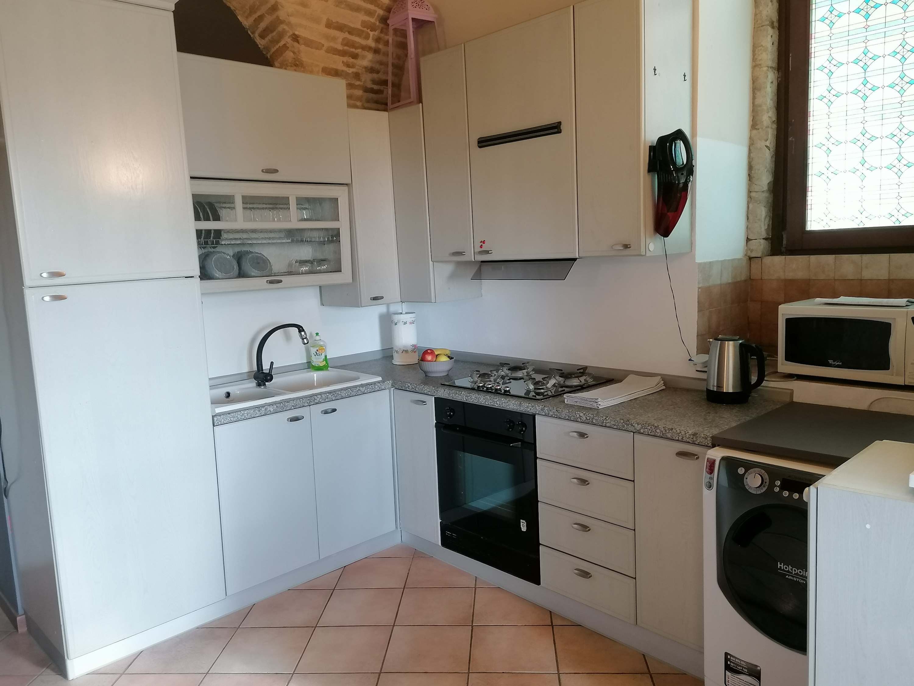 Cozinha com armários brancos, pia, fogão, micro-ondas e máquina de lavar.