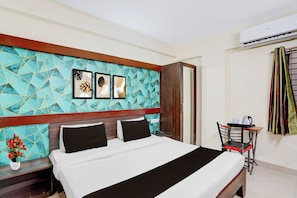 A hotel room with a bed, a small table with a chair, and a wall with geometric-patterned tiles and framed artwork. - Collection O Meghdoot Garden (Indore)