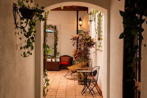 Un espai interior amb terra de rajola, una cadira de vimet, una taula petita i plantes penjants.