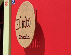 Un senyal de forma circular amb el nom 'El Nito' i 'Fonda' sobre un mur vermell, amb el número de porta '416' visible a l'esquerra.