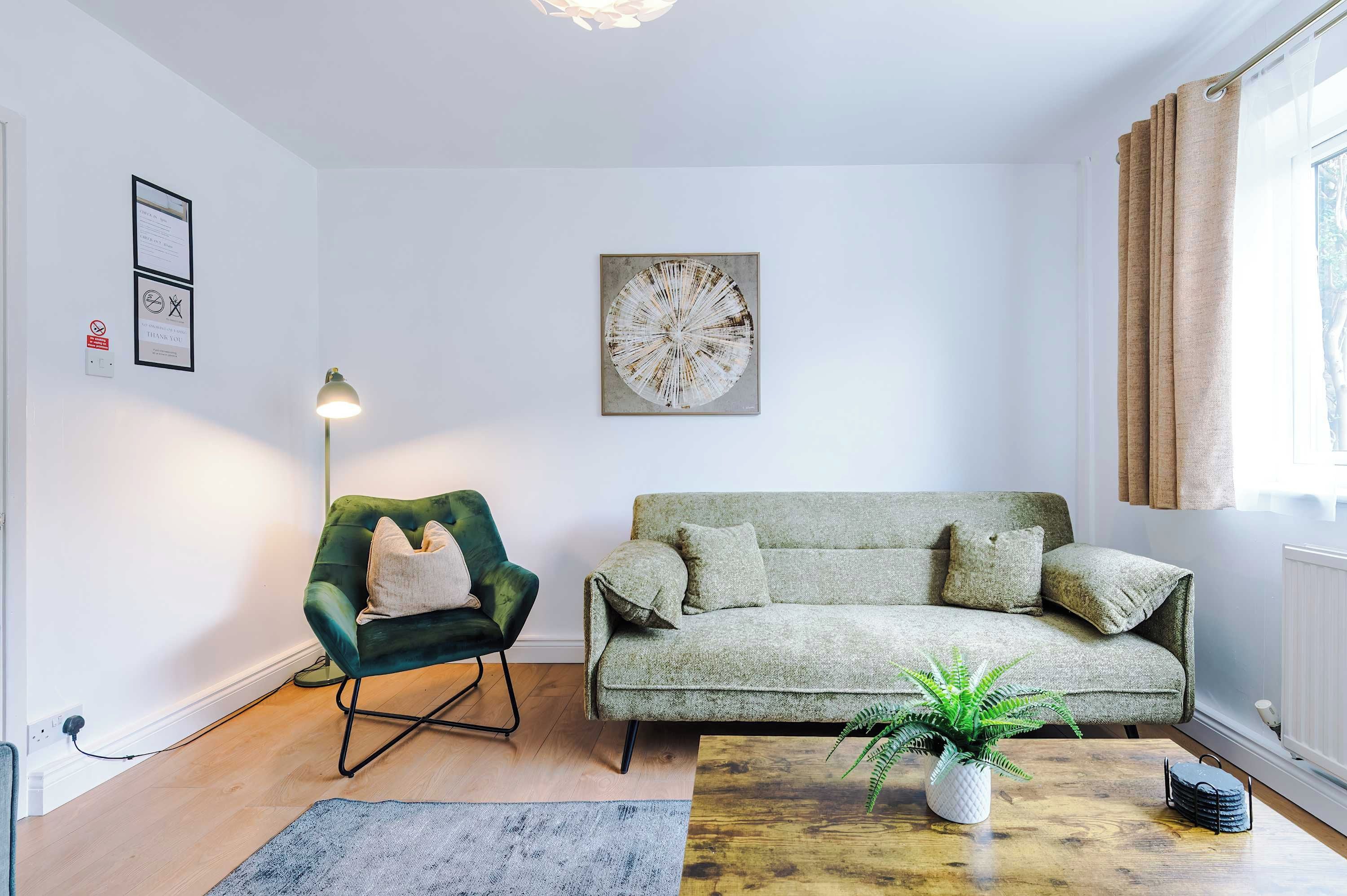 A living room with a green armchair, a grey sofa, a floor lamp, and a wall-mounted artwork.