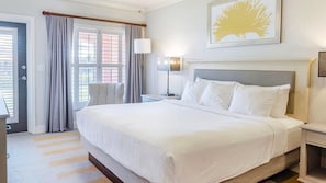 Ein Hotelzimmer mit einem großen Bett, einem Nachttisch, einer Lampe, einem Sessel und einem Fenster mit Vorhängen.
