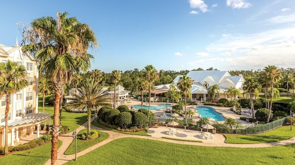 Ein Resort mit Swimmingpool, Palmen und einem großen Gebäude mit weißer Fassade.