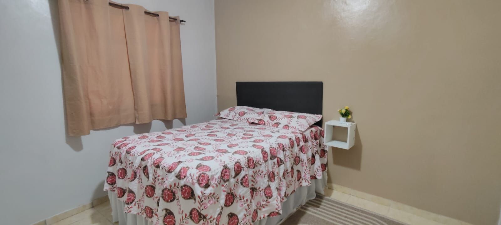 A bedroom with a bed, a nightstand, and a wall-mounted shelf.