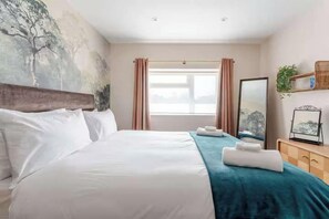 Ein Hotelzimmer mit einem großen Bett, einem Nachttisch, einem Spiegel, einem Fenster mit Vorhängen und einem Wandbild.