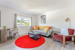 A modern living room with a sofa, a coffee table, and a red rug. - Crawley 1BR | Modern Apartment F2 | Three Bridges (London)