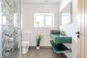 Et badeværelse med toilet, et grønt vaskeskab, et spejl og et vindue.