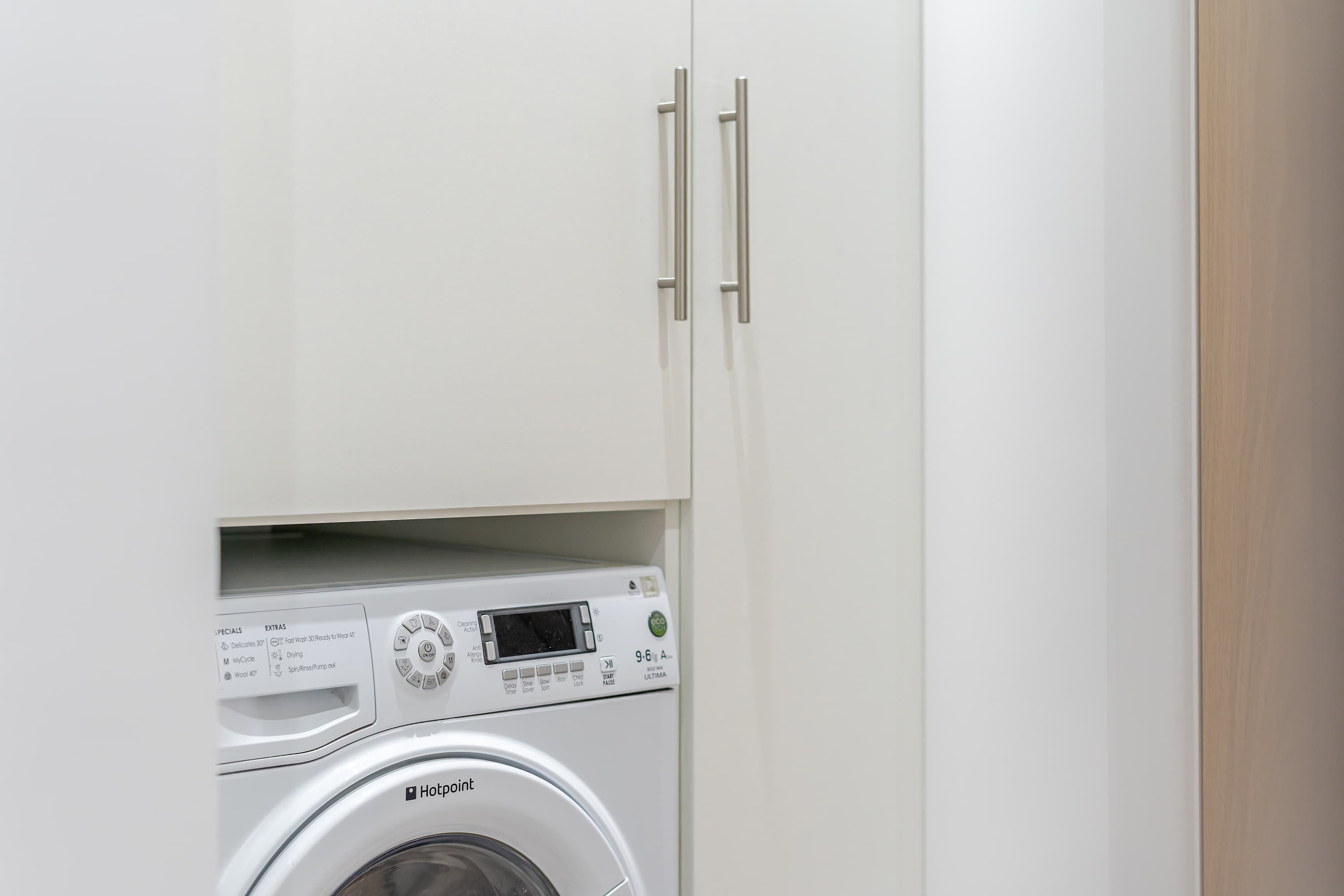 A compact, white washing machine with a digital display and control panel, housed in a minimalist cabinet with a wooden finish.