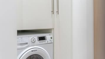 A compact, white washing machine with a digital display and control panel, housed in a minimalist cabinet with a wooden finish.