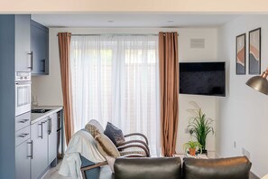 A modern kitchen with a built-in oven and a dining area with a sofa and a coffee table. - Stylish 1 bedroom flat in Crawley (London)