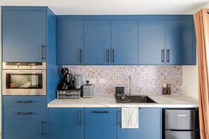 A modern kitchen with blue cabinets, a stainless steel oven, a coffee maker, and a toaster. - Stylish 1 bedroom flat in Crawley (London)