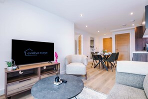 A modern living room with a flat-screen TV, a dining area with a table and chairs, and a kitchen area with a refrigerator and cabinets. - 1BR | Free Wi-Fi | Central Stay | Richmond Hill (Leeds)