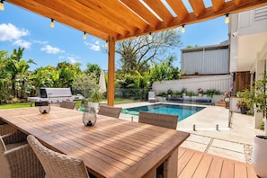 An outdoor patio with a wooden table and chairs, a barbecue grill, and a swimming pool. - Solara Studio at Corlette (Corlette)