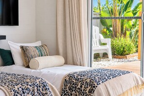 Habitación de hotel con cama, dos almohadas, ventana con cortinas y vista a un jardín.