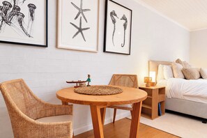 A bedroom with a bed, two wicker chairs, a small table with a decorative item, and three framed artworks on the wall. - Solara Studio at Corlette (Corlette)
