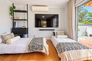 A bedroom with two beds, a TV, a shelf with plants, and a view of the outdoors. - Solara Studio at Corlette (Corlette)