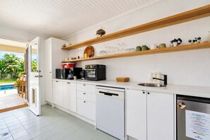 A modern kitchen with white cabinetry, wooden shelves, and a built-in dishwasher. - Solara Studio at Corlette (Corlette)