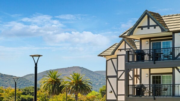 A two-story building with a balcony, a mountain backdrop, and a clear sky.