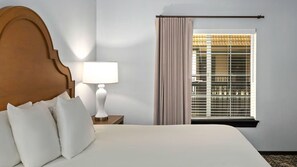 A hotel room with a bed, a nightstand, a lamp, and a window with blinds.