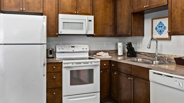 A kitchen with wooden cabinets, a white refrigerator, a microwave, a stove, and a sink.
