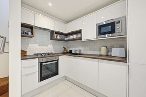 A modern kitchen with white cabinetry, a built-in oven, a gas stove, a microwave, and a kettle. - Garden Duplex with 2 Baths - West Didsbury (Manchester)