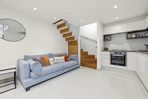 A modern living space with a sofa, a wooden staircase, and a kitchen area. - Garden Duplex with 2 Baths - West Didsbury (Manchester)