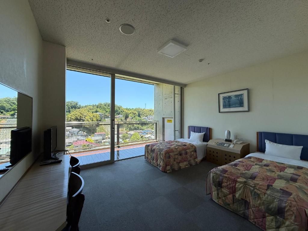 Habitación de hotel con dos camas, un escritorio, televisión y balcón con vista a la ciudad.