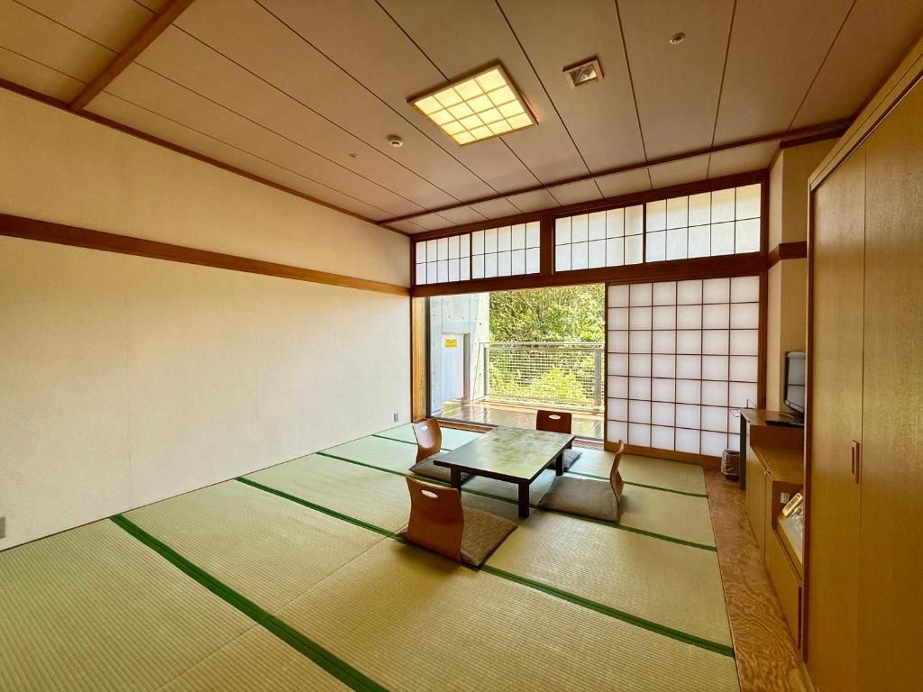 Una habitación con esteras tatami, una mesa baja, sillas, un televisor y una puerta corredera.