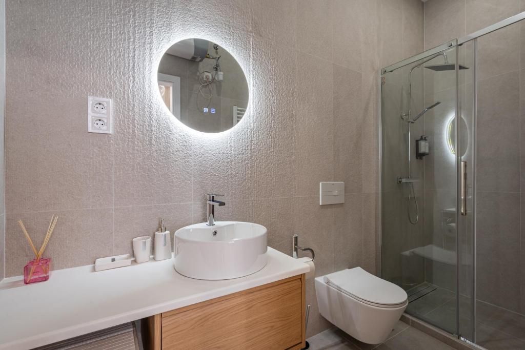 Ein modernes Badezimmer mit rundem Spiegel, Waschbecken, Toilette und Duschkabine aus Glas.