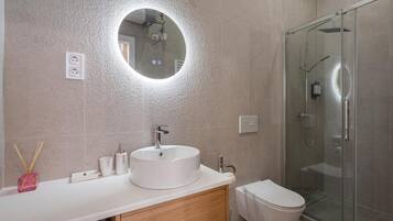 Ein modernes Badezimmer mit rundem Spiegel, Waschbecken, Toilette und Duschkabine aus Glas.