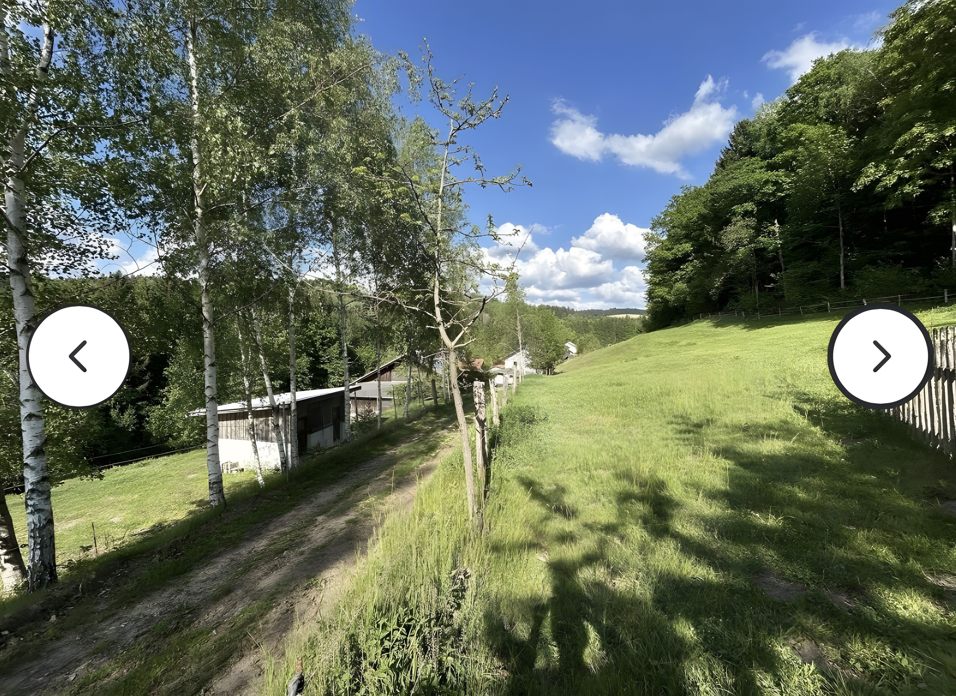 Ländliche Landschaft mit einem Feldweg, Holzzaun und einem kleinen Gebäude.