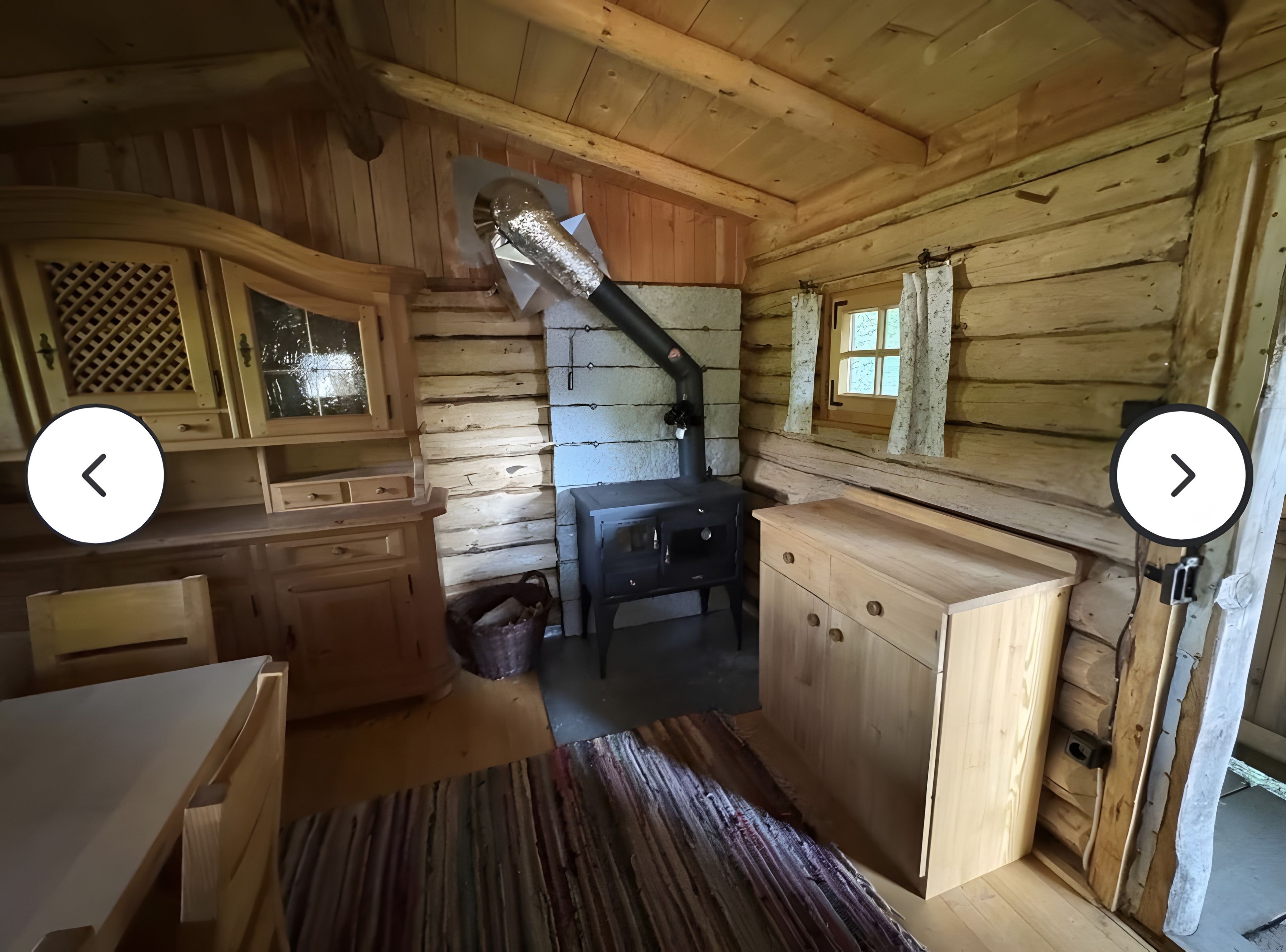 L’intérieur d’un chalet en bois rustique, avec une cheminée, des armoires en bois et une fenêtre avec des rideaux.