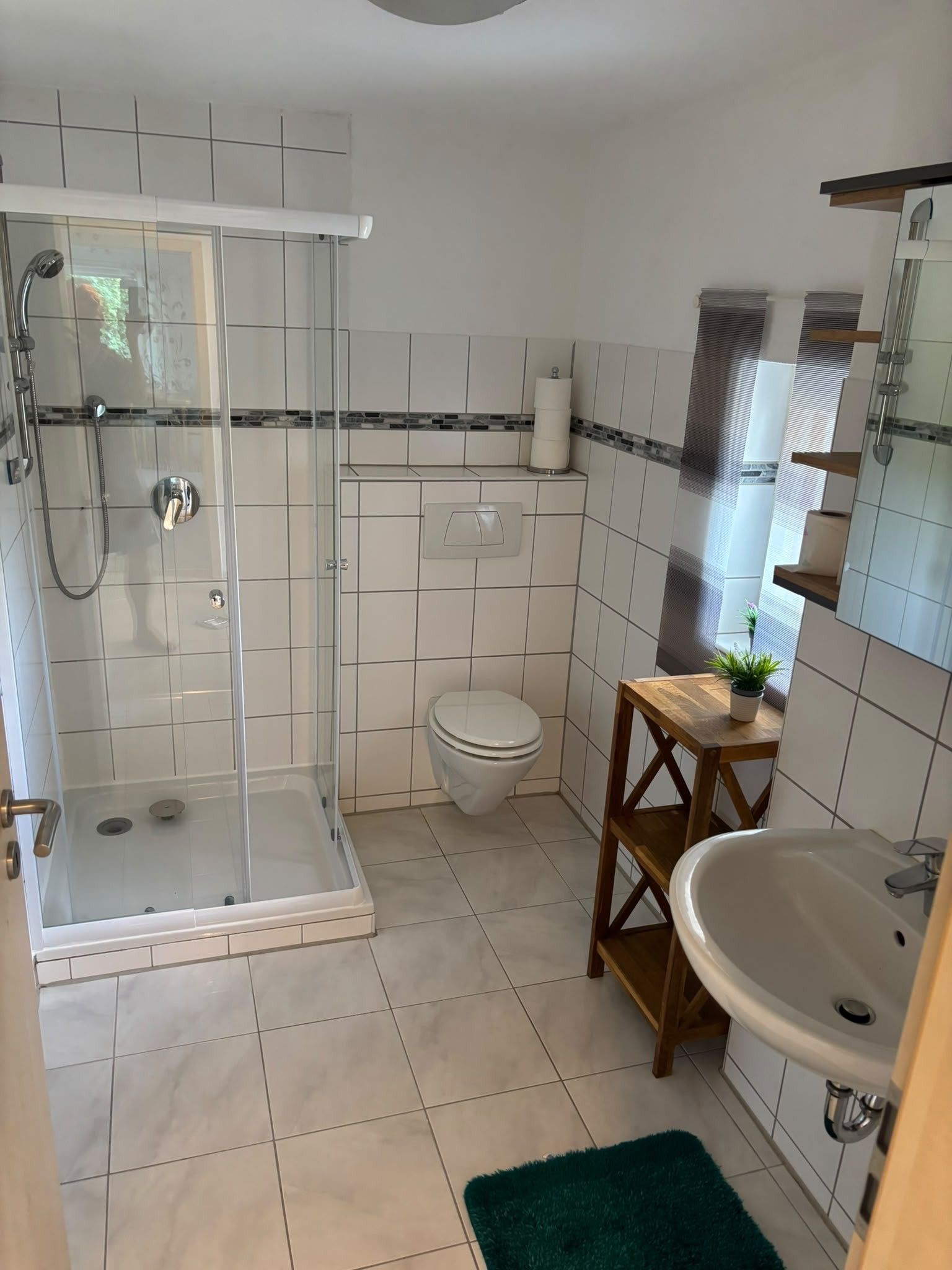 Ein Badezimmer mit Duschkabine, Toilette, Waschbecken und einem kleinen Holzschemel.