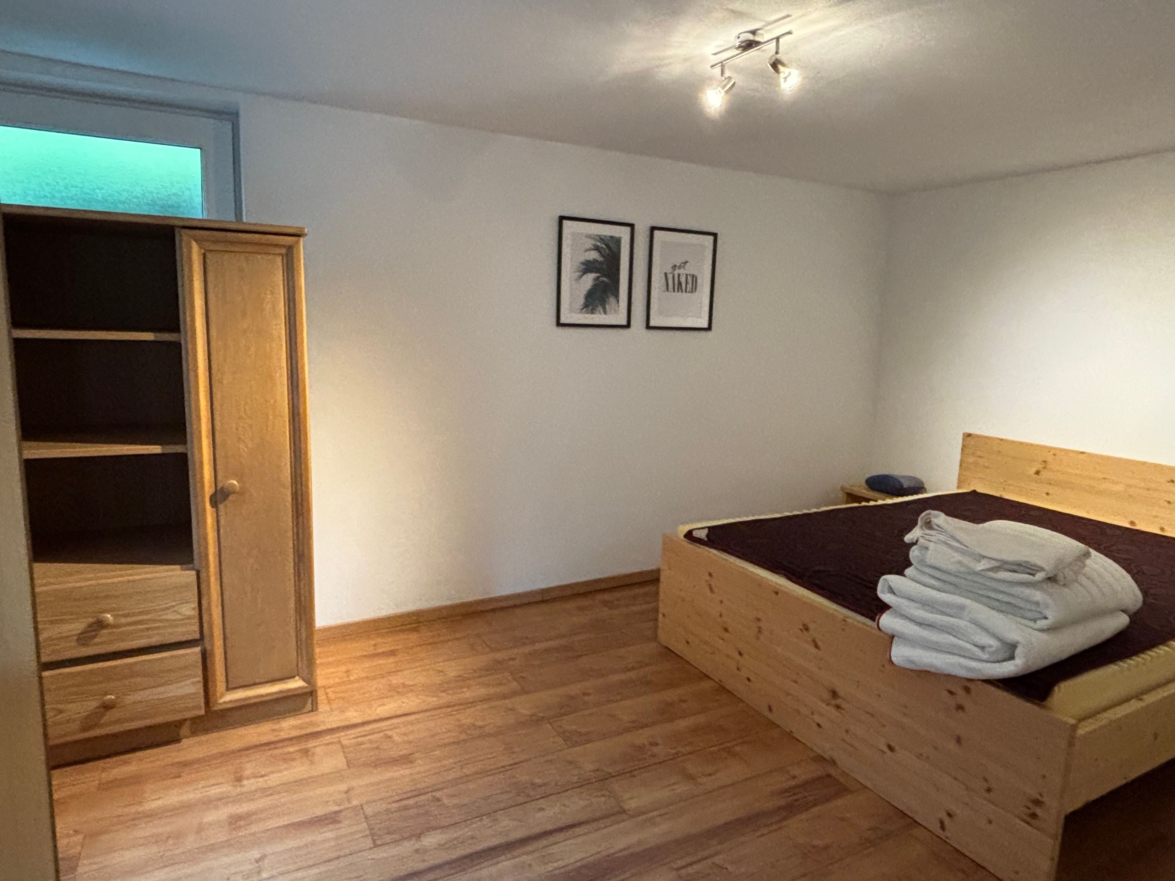 A bedroom with a wooden bed, a wardrobe, and two framed pictures on the wall.