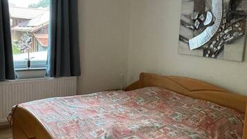 Ein Schlafzimmer mit einem Bett, einem Deckenventilator, einem Fenster mit Vorhängen und einem an der Wand befestigten Kunstwerk.