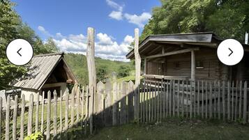 Ein rustikales Holzhäuschen mit eingezäunter Wiese, umgeben von Bäumen und Hügeln.